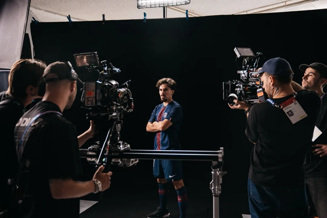 Two camera operators filming a PSG player against a black studio backdrop
