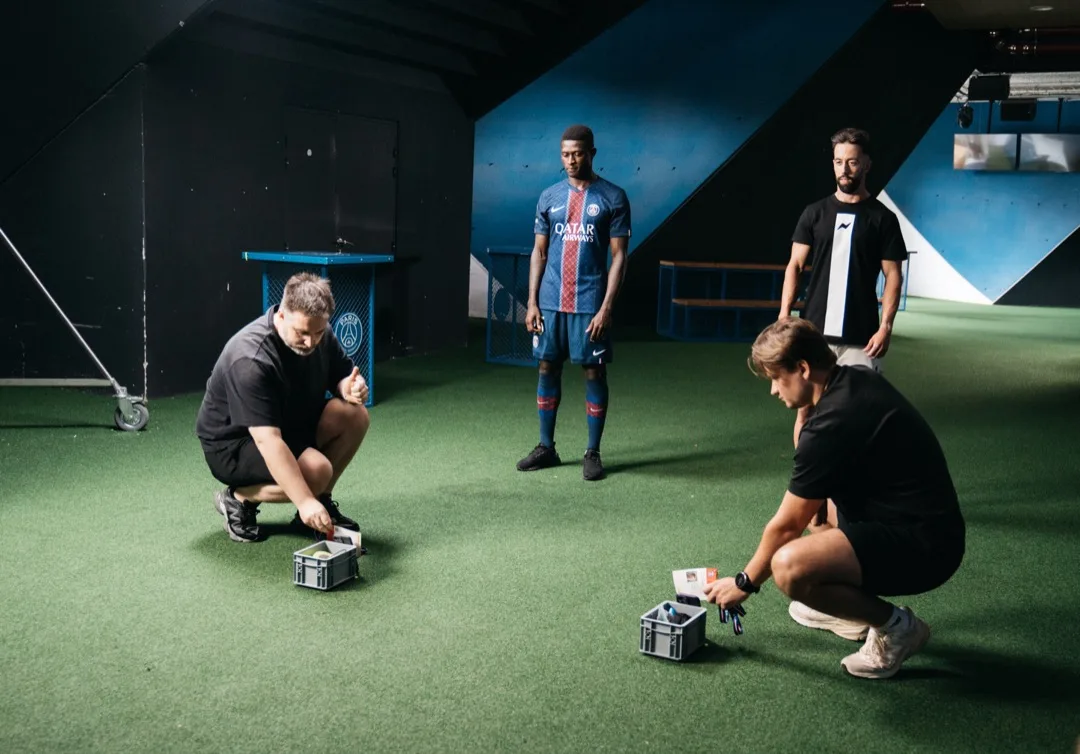 Crew placing exercise markers on the pitch-side turf while a PSG player waits on set