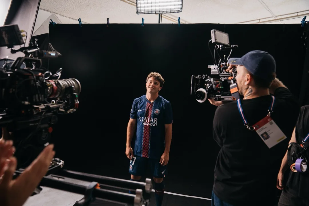 A smiling PSG player on the black studio set, camera rig in the foreground